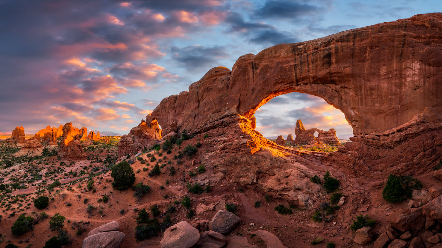 Turret Arch A natural sandstone arch frames a desert landscape at sunset, with rugged rock formations and a colorful sky