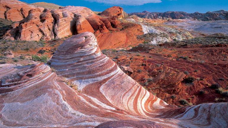 A colorful, layered rock formation in a desert landscape under a clear blue sky in Valley of Fire State Park.