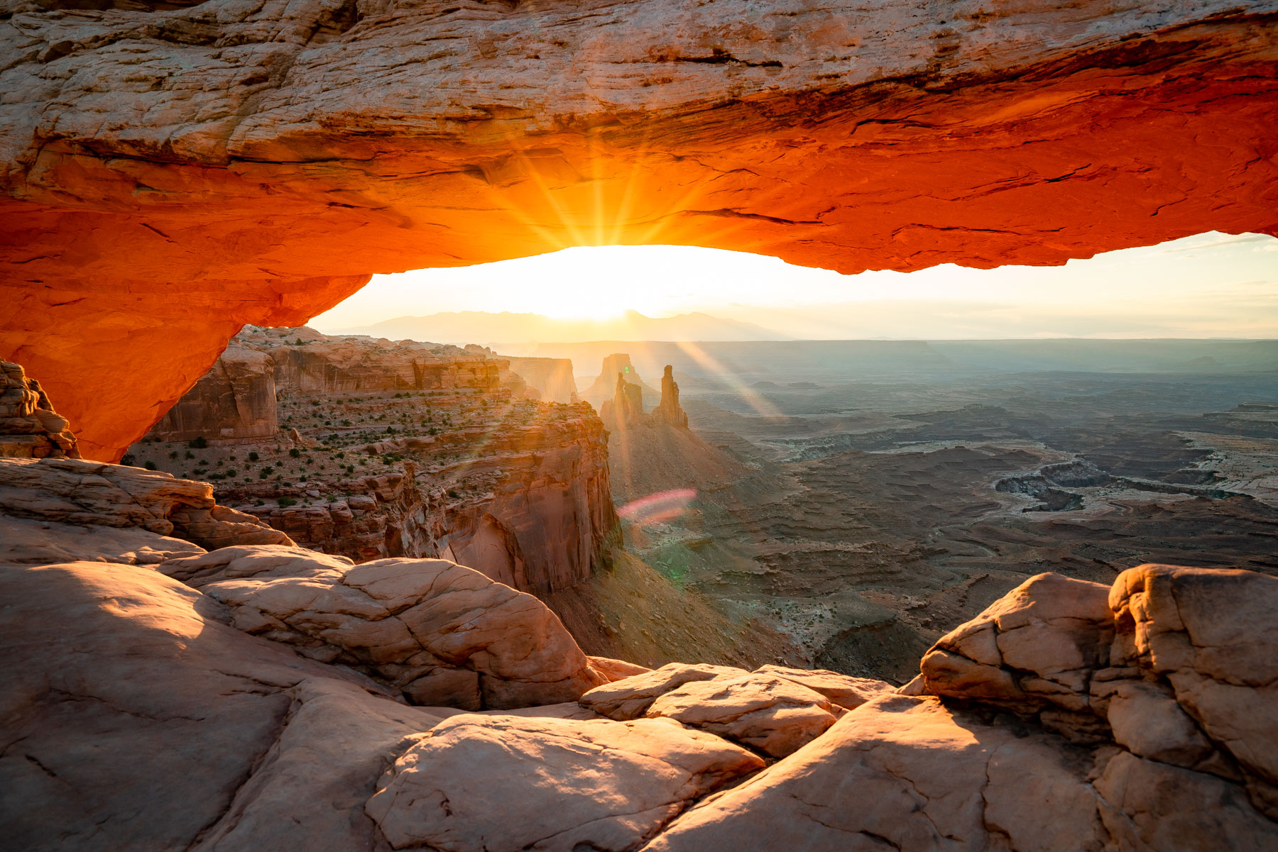 Mesa Arch in Canyonlands National Park at sunrise, framing the canyon and mountains in the distance.