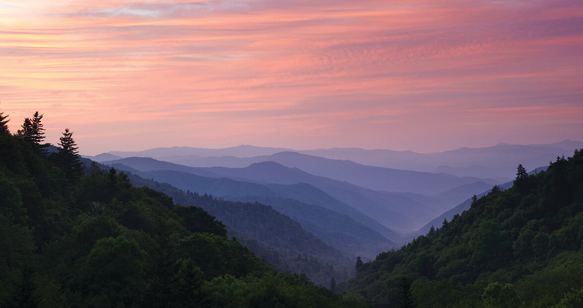 Rolling mountains under a vibrant orange, pink, and purple sunset sky.